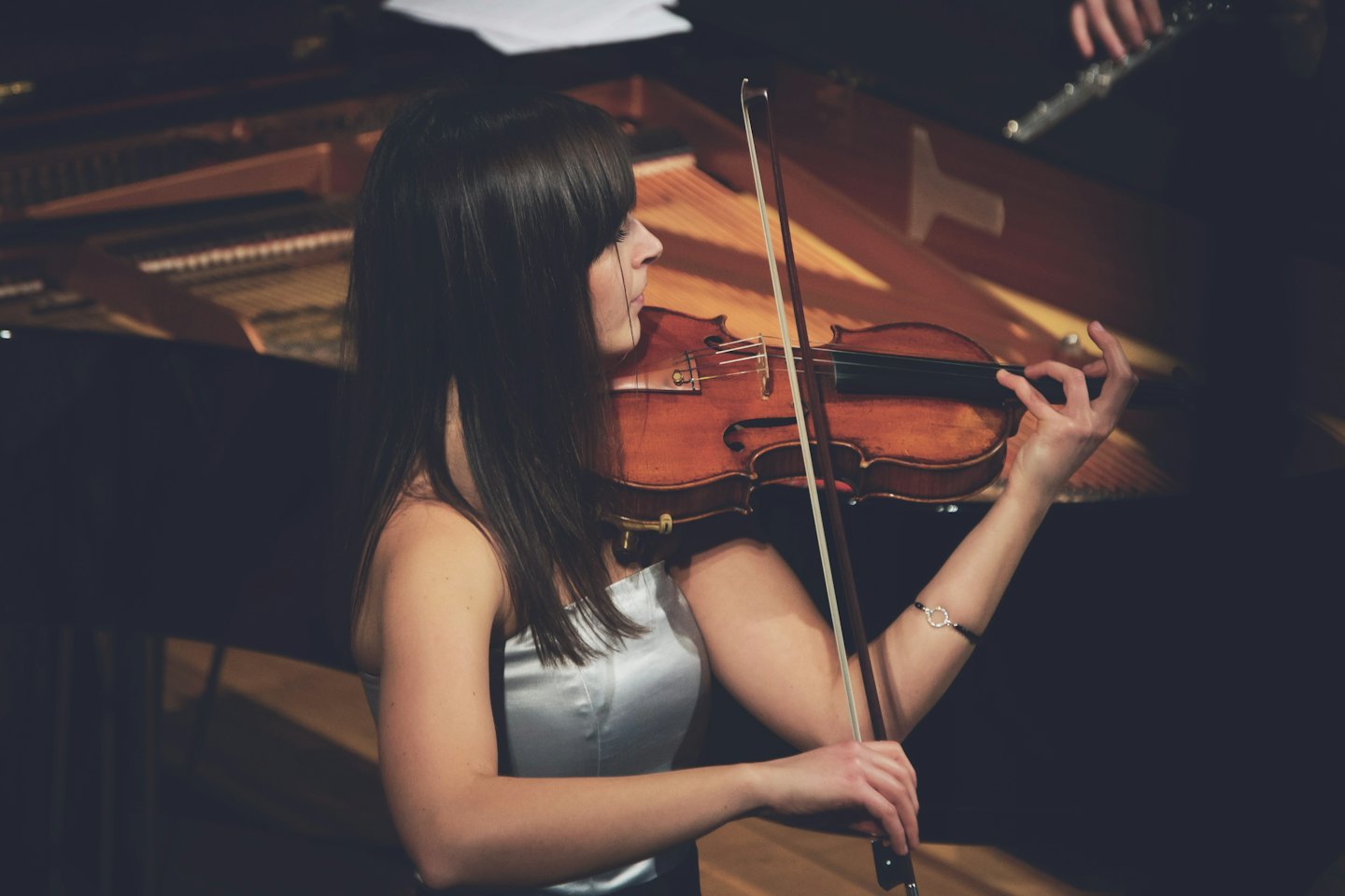Woman playing violin with piano and flute in background.