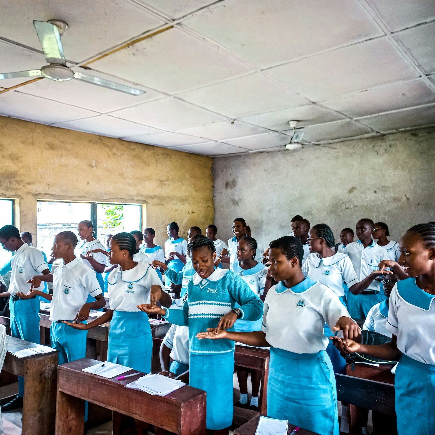 Students in uniform perform synchronized hand gesture in a classroom.