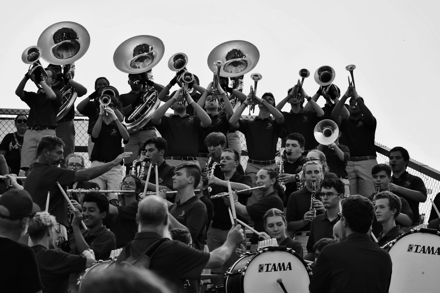 Diverse young musicians play brass and percussion instruments in an outdoor band practice.