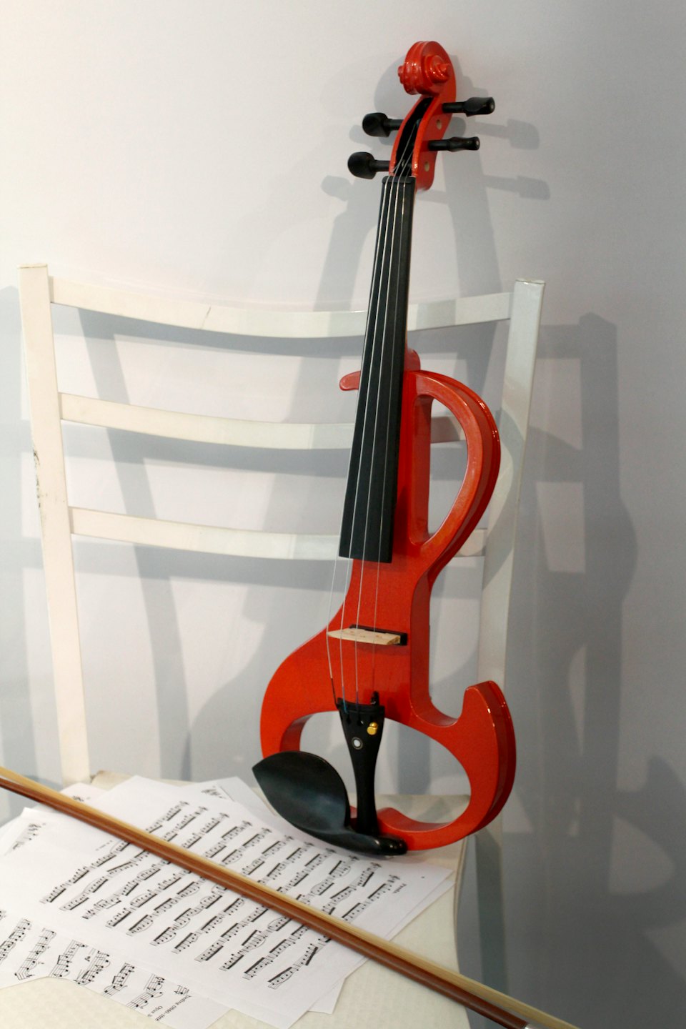 A red electric violin leans against a wooden chair with sheet music.